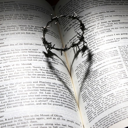 Circle of thorns casting heart shaped shadow on open bible